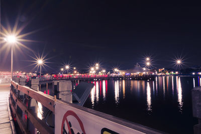 Illuminated city by river against sky at night