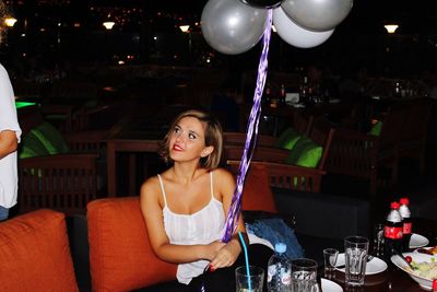 Beautiful woman holding helium balloons while sitting at restaurant