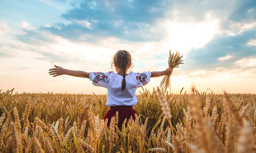 Rear view of girl holding wheat crops standing on field