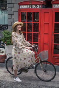 Beautiful caucasian young woman in dress, sneakers and straw hat riding a bicycle in london