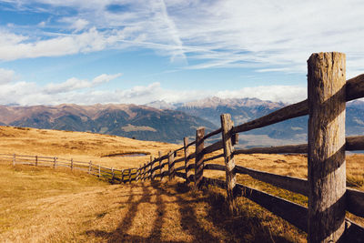 Wooden fence on field by mountains against sky