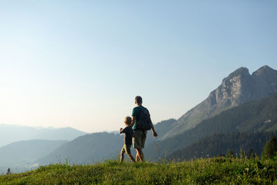 Rear view of man walking on mountain against clear sky