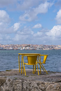 Chair on table by sea against sky in city