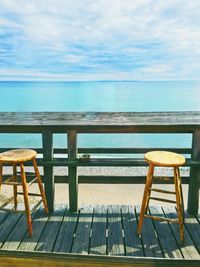 Chairs and table by sea against sky