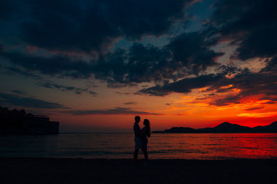 Silhouette friends standing on beach against sky during sunset