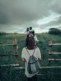 Rear view of woman photographing on field against sky