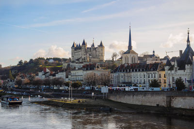 Sailboats in river by buildings in city against sky