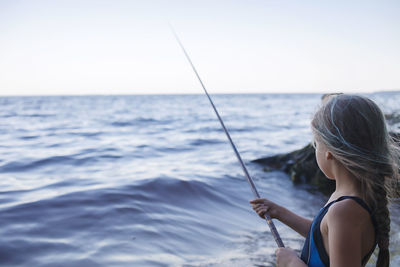 Woman holding fishing rod by sea against sky