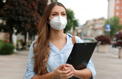 Young woman looking away while holding file in city