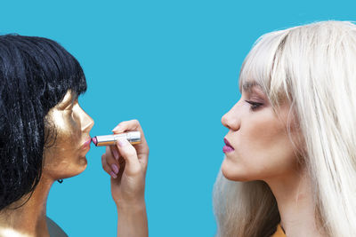 Close-up of woman applying lipstick to mannequin against blue background