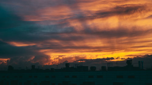 Silhouette buildings against dramatic sky during sunset