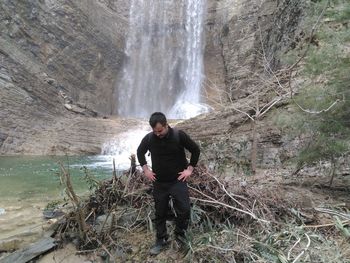 Man looking down while standing by waterfall