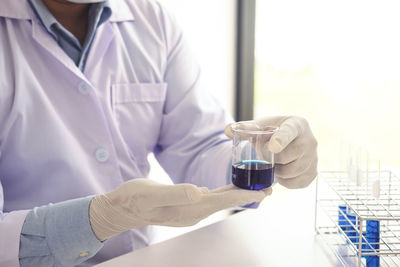 Midsection of scientist holding chemical in beaker at laboratory