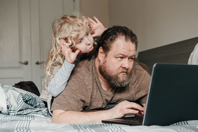Work from home with kids. father working on laptop in bedroom with child daughter on his back