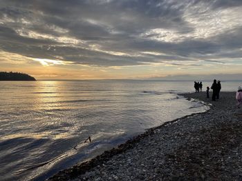 People on beach against sky during sunset