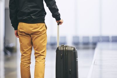 Midsection of young man with luggage standing by conveyor belt at airport