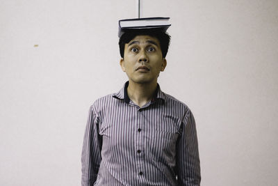 Mid adult man balancing book on head while standing against wall