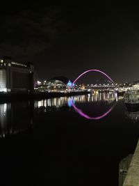 Illuminated city by river against sky at night