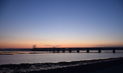 Silhouette bridge over sea against sky during sunset