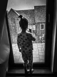 Rear view of girl standing by window at home