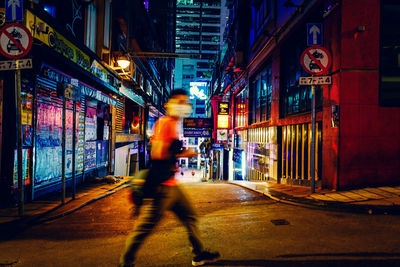 Blurred motion of man walking on illuminated street at night