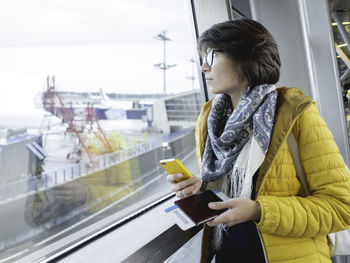 Woman with passport and boarding pass is texting on her smartphone. tourist is waiting for boarding