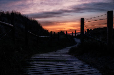 Boardwalk against cloudy sky at sunset