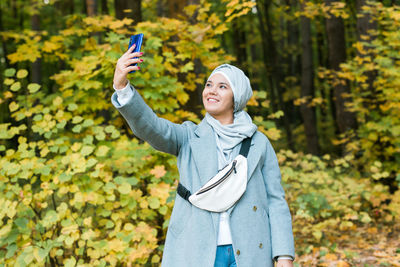 Full length portrait of smiling young woman using mobile phone