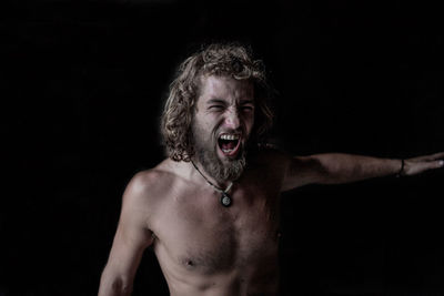 Portrait of shirtless young man against black background