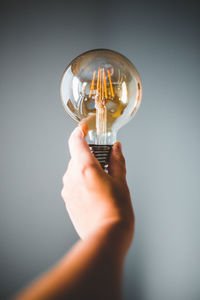 Close-up of hand holding light bulb against gray background