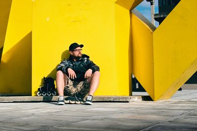 Bearded man with glasses and his roller blades sitting by the yellow statue