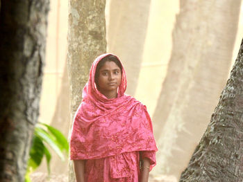 Portrait of young woman standing against trees 