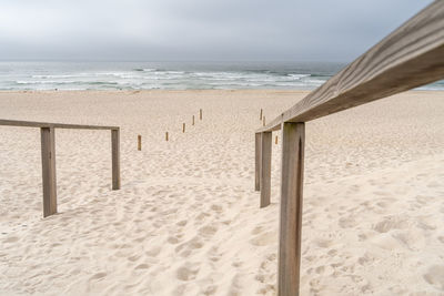 Wooden railings on the sand directing you to the beach on a cloudy day in costa nova, portugal.