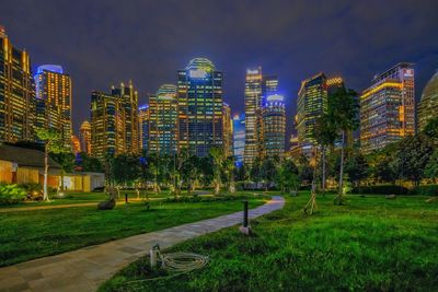 Illuminated park by buildings against sky at night