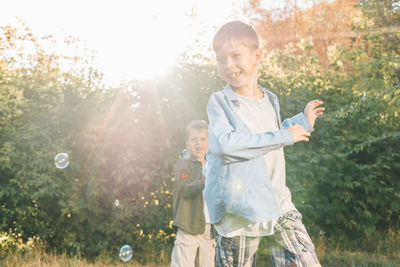 A boy is playing with soap bubbles in a summer park, among the greenery.