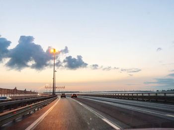 Vehicles on road against sky during sunset