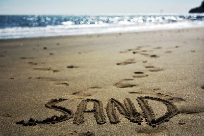 Text written on sand at beach against sky