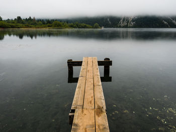 Wooden post on pier by lake against sky