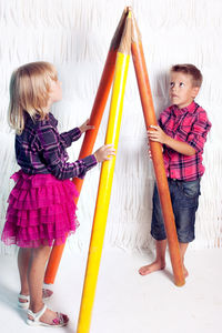 Siblings with large pencils standing against curtain