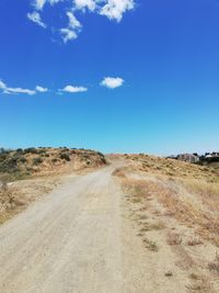 Dirt road passing through landscape against blue sky