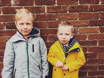 Portrait of smiling siblings standing against brick wall