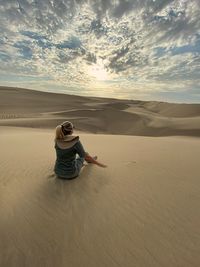 Rear view of woman sitting at desert during sunset