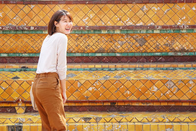 Full length portrait of smiling young woman standing outdoors