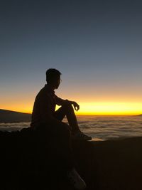 Side view of silhouette man sitting on beach against sky during sunset