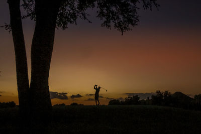 Silhouette man playing golf on field against sky during sunset