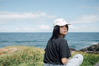 Portrait of young woman looking at sea against sky