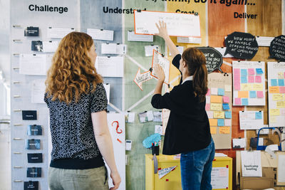 Female colleagues discussing over strategy on wall at creative office