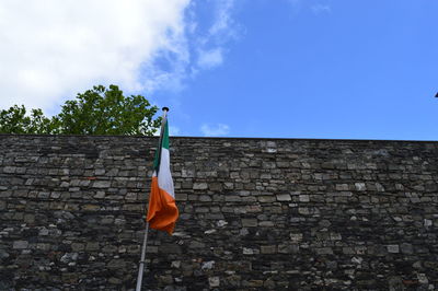Low angle view of irish flag by stone wall against sky