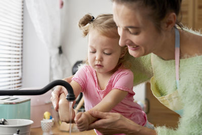 Smiling mother washing daughter hands at sink