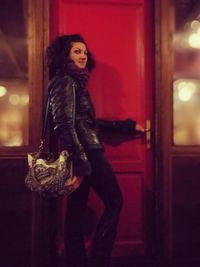 Portrait of young woman standing against door at night